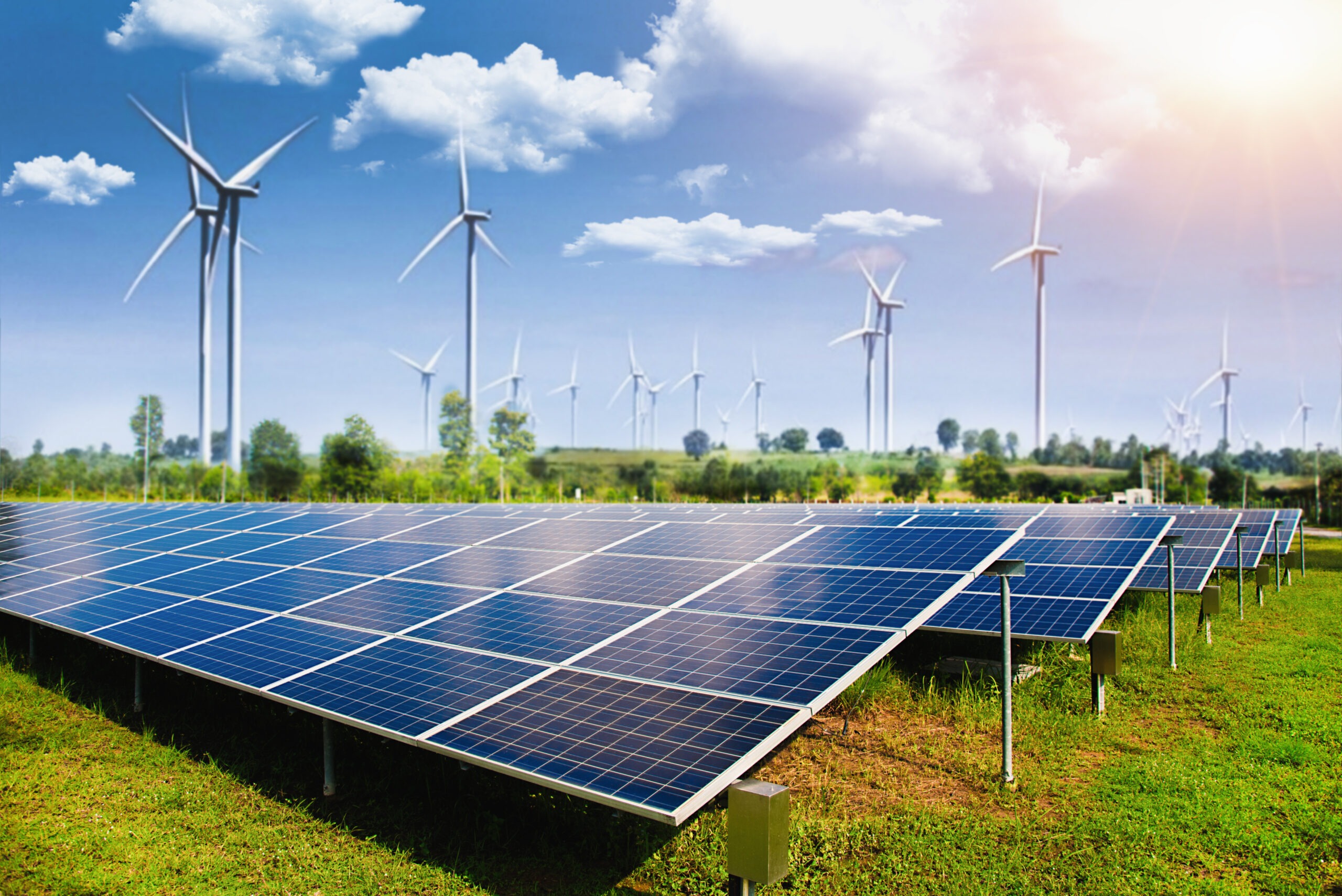 Solar panels in the foreground with wind turbines in the background, illustrating a renewable energy landscape under a bright sky.